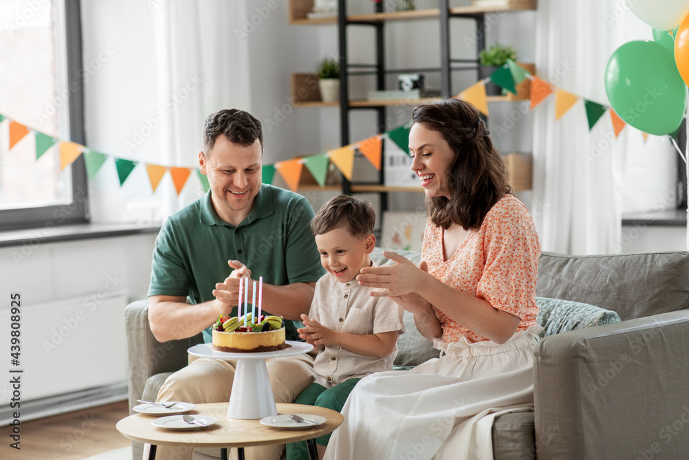 family, holidays and people concept - portrait of happy mother, father and little son with four candles on birthday cake clapping hands at home party party