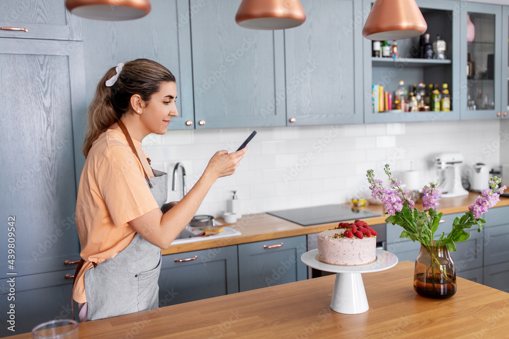 culinary, baking and cooking food concept - happy smiling young woman with smartphone taking picture of raspberry cake on kitchen at home culinary, baking and cooking food concept - happy smiling young woman with smartphone taking picture of raspberry cake on kitchen at home