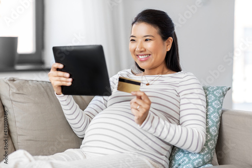 pregnancy, online shopping and people concept - happy smiling pregnant asian woman with tablet pc computer and credit card sitting on sofa at home