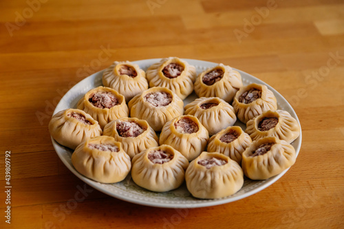 Steamed national Mongolian food dumpling Buuz filled with minced beef, white plate, wooden table, Close up east Siberian Buryats dish poses, Juicy minced meat wrapped handmade dough shirt buuza