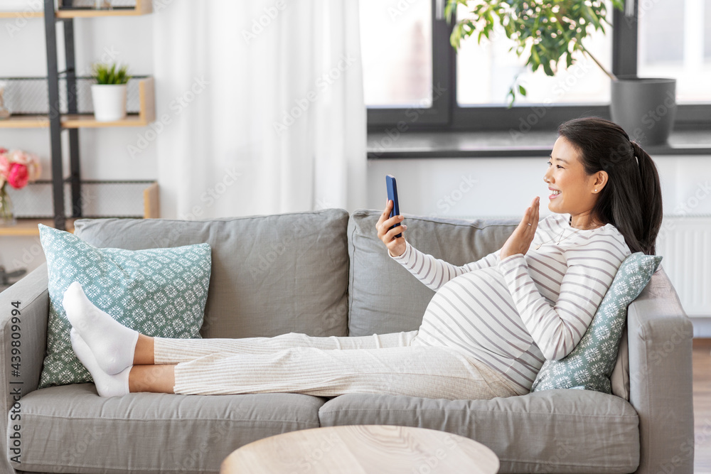 pregnancy, rest, people and expectation concept - happy smiling pregnant asian woman sitting on sofa at home having video call on smartphone pregnancy, rest, people and expectation concept - happy smiling pregnant asian woman sitting on sofa at home having video call on smartphone