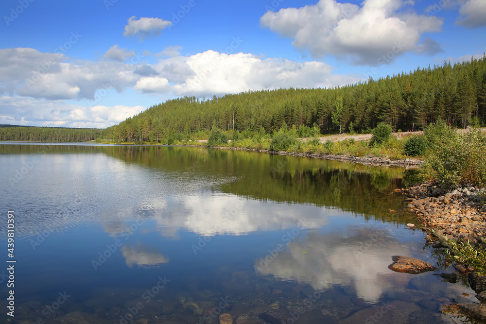 Beautiful landscape with a calm clear lake which has reflections of the trees and clouds. The lake lies within the Arctic circle near Polcirkeln, Northern Sweden, Scandinavia.