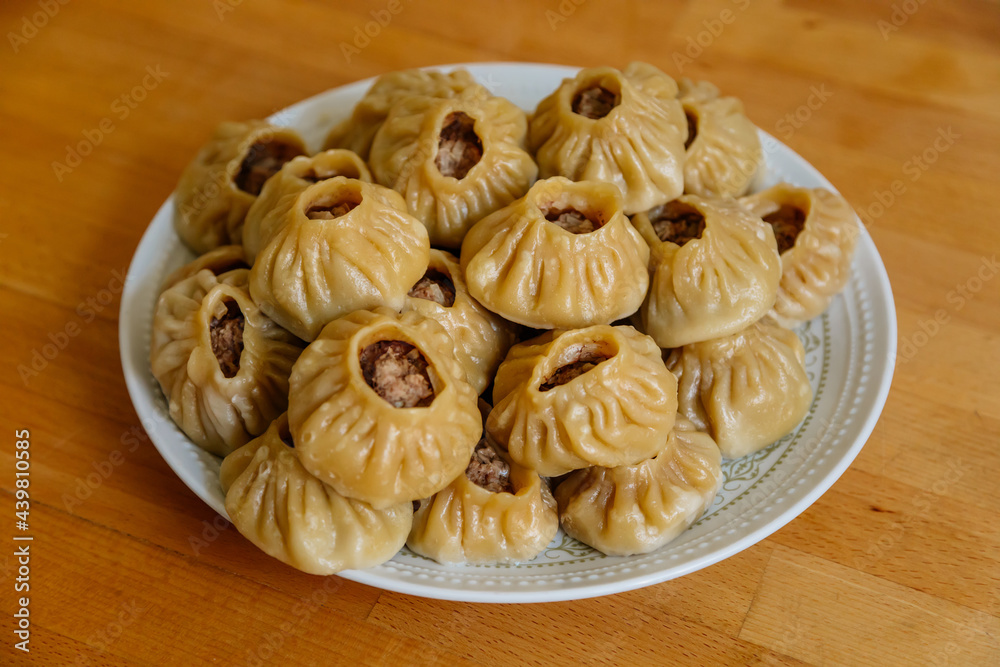 Steamed national Mongolian food dumpling Buuz filled with minced beef, white plate, wooden table, Close up east Siberian Buryats dish poses, Juicy minced meat wrapped handmade dough shirt above view