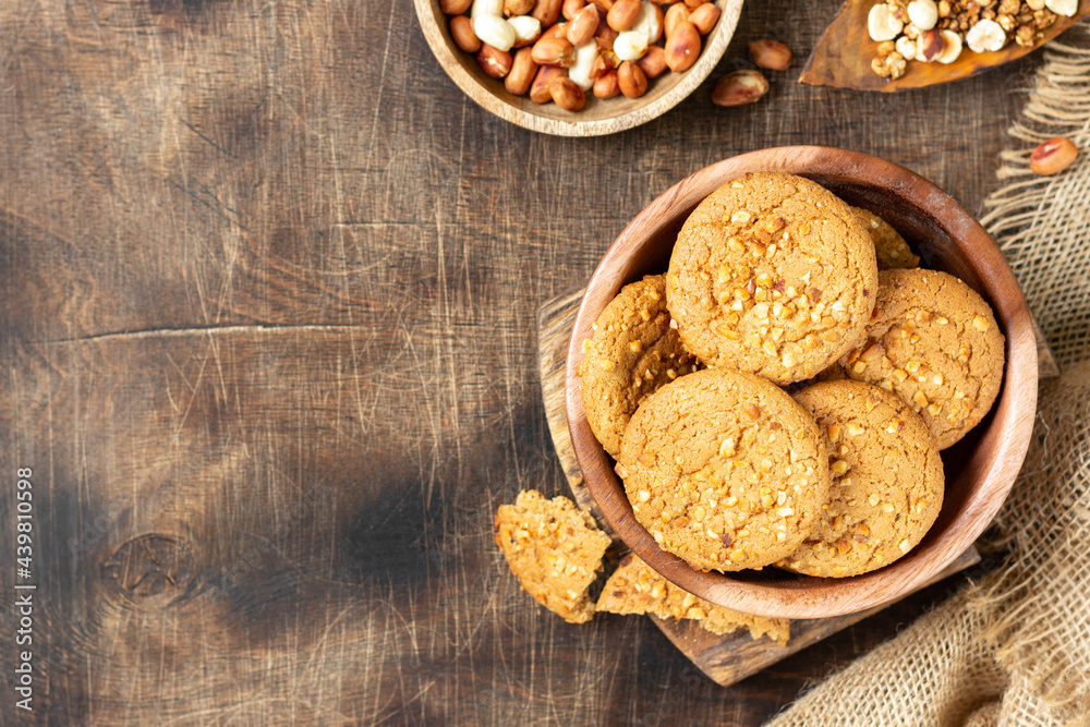 Healthy homemade oatmeal cookies with peanuts in a wooden bowl on a brown kitchen table top view with copyspace