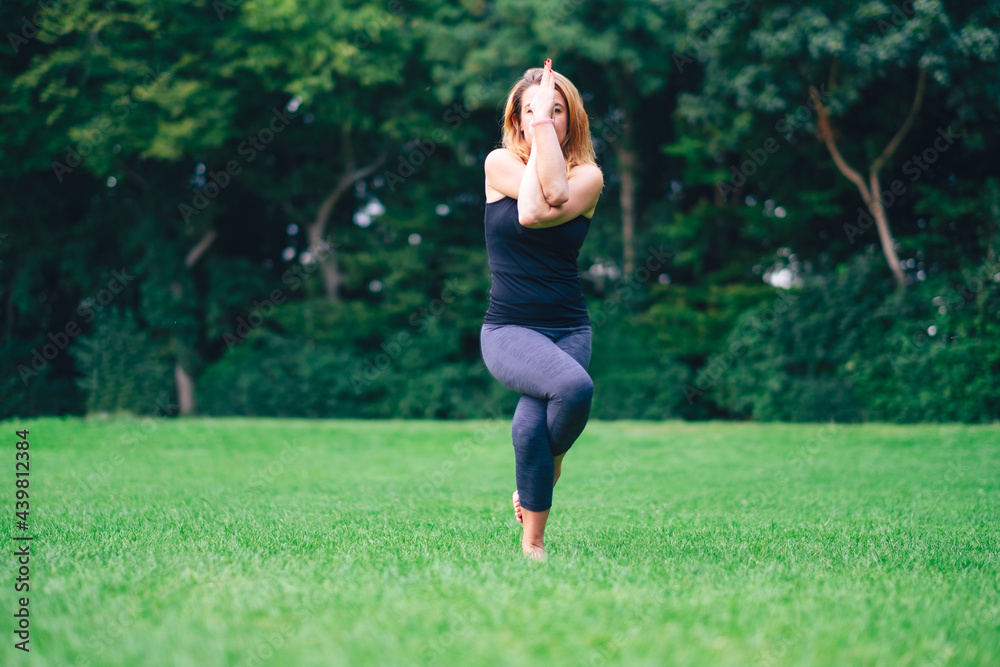 woman in park practicing yoga in nature on grass with barefoot