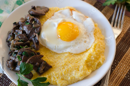 Corn porridge, fried egg, fried mushrooms with onions in a plate on a wicker bamboo napkin.