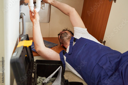 Handyman repairs defective siphon in the kitchen sink photo