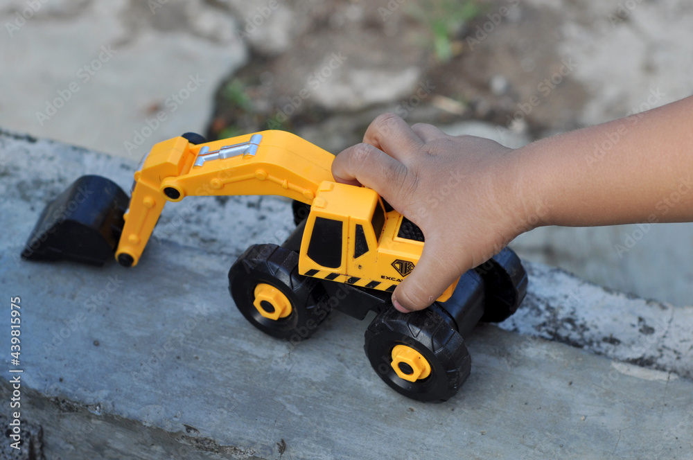 Children holding yellow excavator vehicle toy outdoor