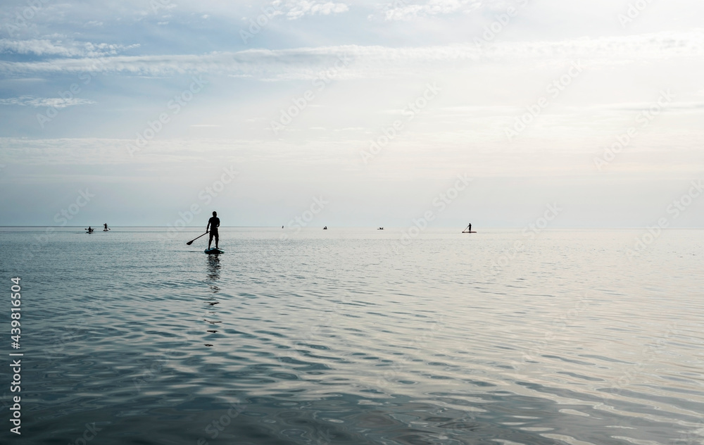 Fototapeta premium Young man floating on stand up paddle board on the sea on sunny summer day, active lifestyle, outdoor activity