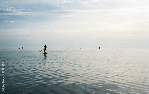 Young man floating on stand up paddle board on the sea on sunny summer day, active lifestyle, outdoor activity