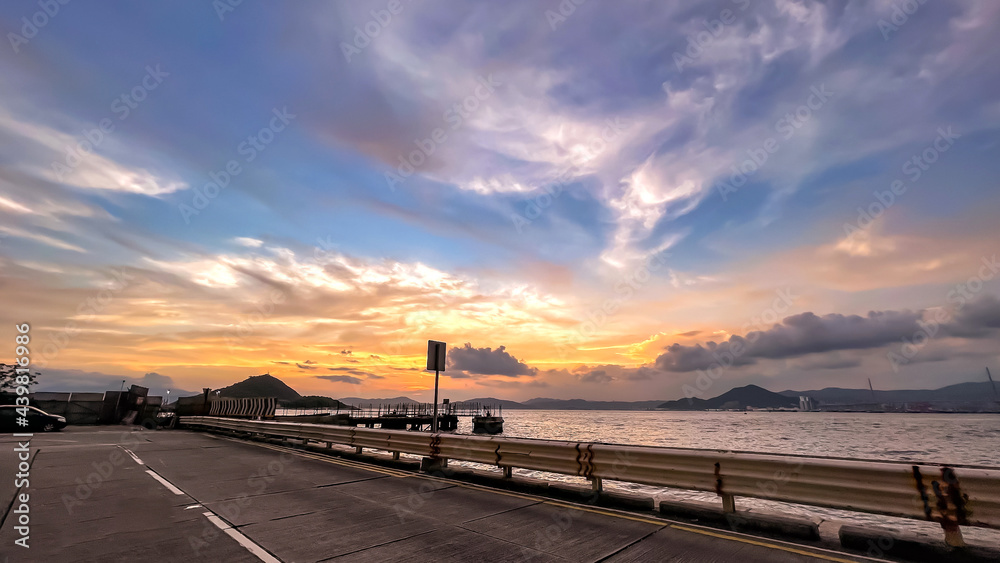 horizontal landscape photograph mountain, road, fence, cloud and ocean at sunset