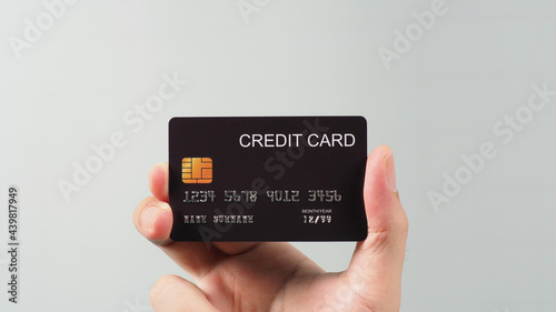 Hand is holding black credit card isolated on grey background.