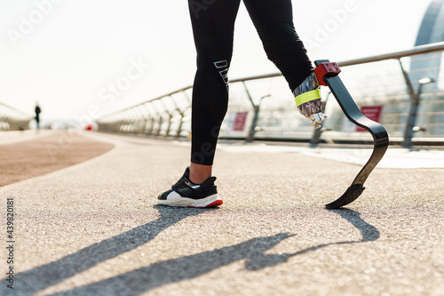 Young sportswoman with prosthesis walking on city bridge