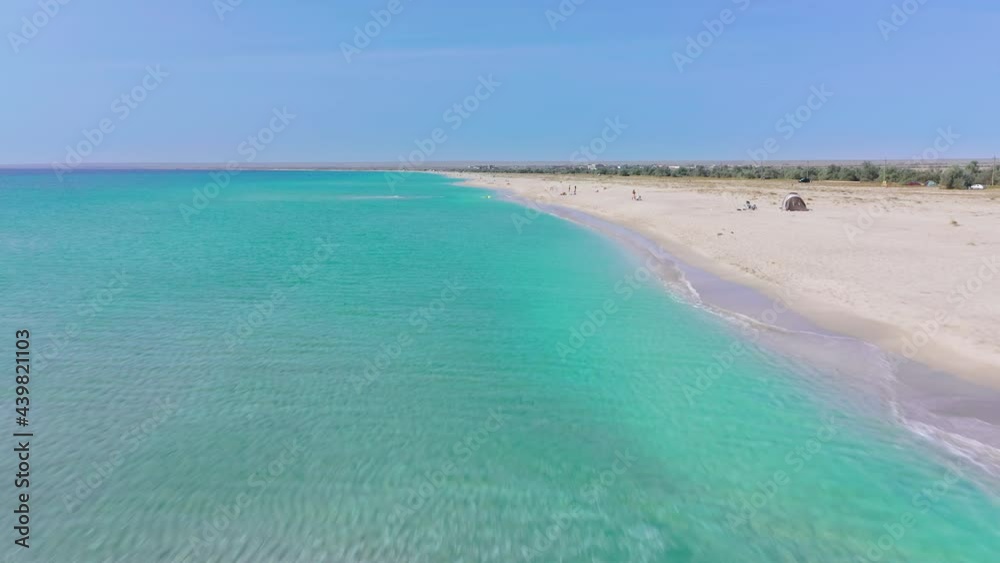 Flying forward over the sea coastline with emerald colored water where people are resting on a white sandy beach on a sunny day Flying forward over the sea coastline with emerald colored water where people are resting on a white sandy beach on a sunny day