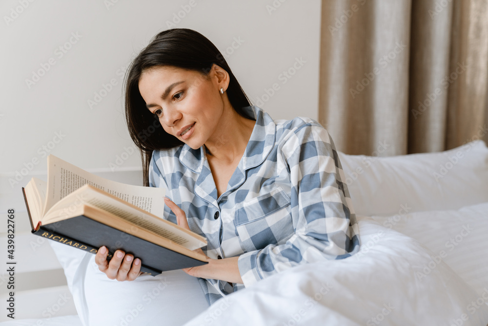 Young hispanic woman reading book while lying in bed at home Young hispanic woman reading book while lying in bed at home
