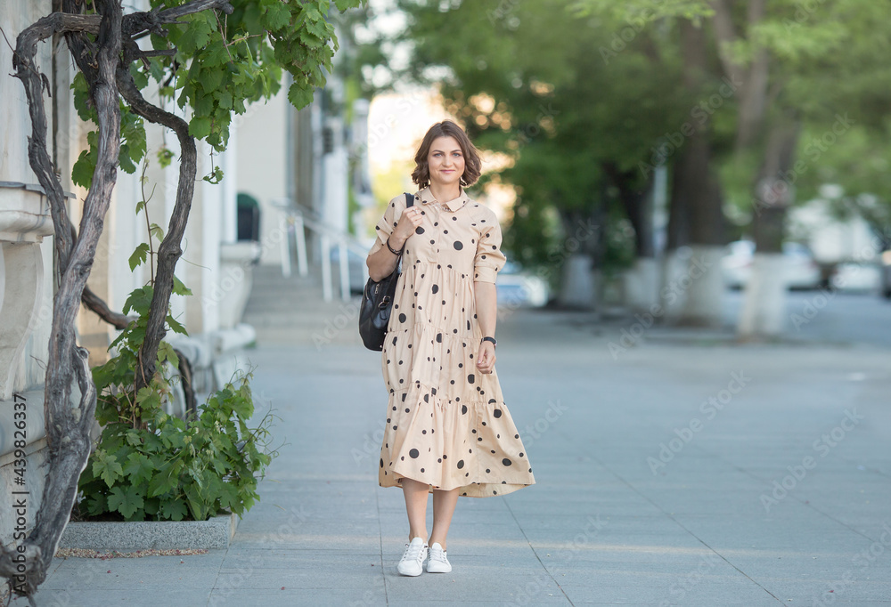 a happy girl is walking in a dress on a city street and smiling.