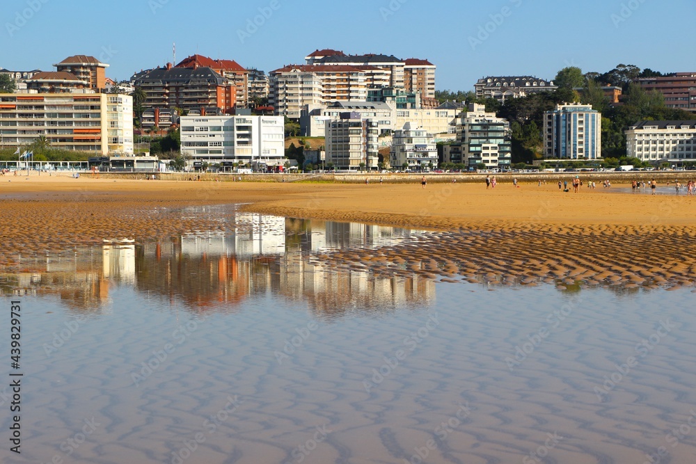 Fototapeta premium View of the beach with reflected buildings in a pool of sea water on a sunny spring June 2021 morning Sardinero Santander Cantabria Spain