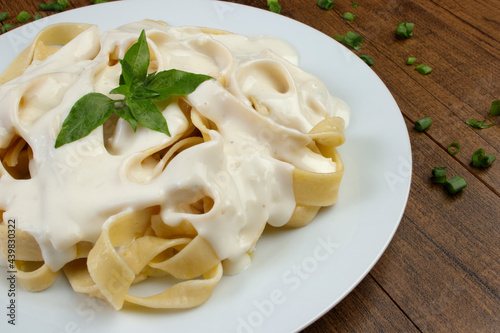 Tagliatelle pasta served with bechamel sauce and basil leaves. Pasta with white sauce. Close-up photography of pasta cuisine.