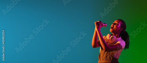 Latino female singer portrait isolated on studio background in neon light. Beautiful female model in black wear with microphone.