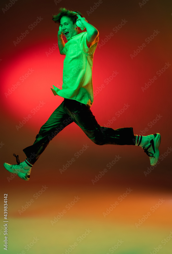 Caucasian young man in headphones isolated on blue studio background in neon. Concept of human emotions, facial expression.