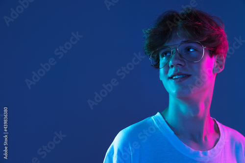 Caucasian young man's portrait on dark studio background in neon. Concept of human emotions, facial expression.