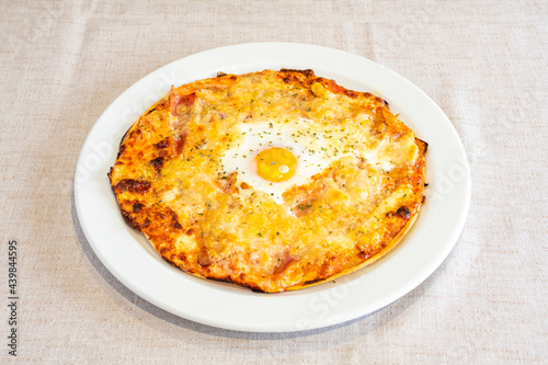 Rustic Italian pizza with a lot of cheese gratin and a fried egg in the middle