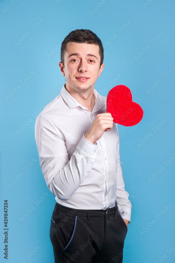 Cute handsome man holdiing red heart made of paper for Valentines Day on blue background Cute handsome man holdiing red heart made of paper for Valentines Day on blue background