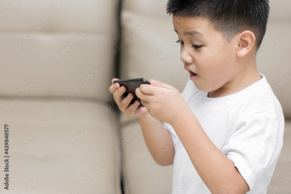 Happy little boy having fun playing game on mobile phone, Preschool kid sitting on sofa with smiling face watching cartoon on smartphone, Child using cell phone while relaxing at home Happy little boy having fun playing game on mobile phone, Preschool kid sitting on sofa with smiling face watching cartoon on smartphone, Child using cell phone while relaxing at home