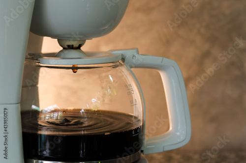 Coffee pot with coffee dripping inside on gray concrete background and warm light. Copy space.