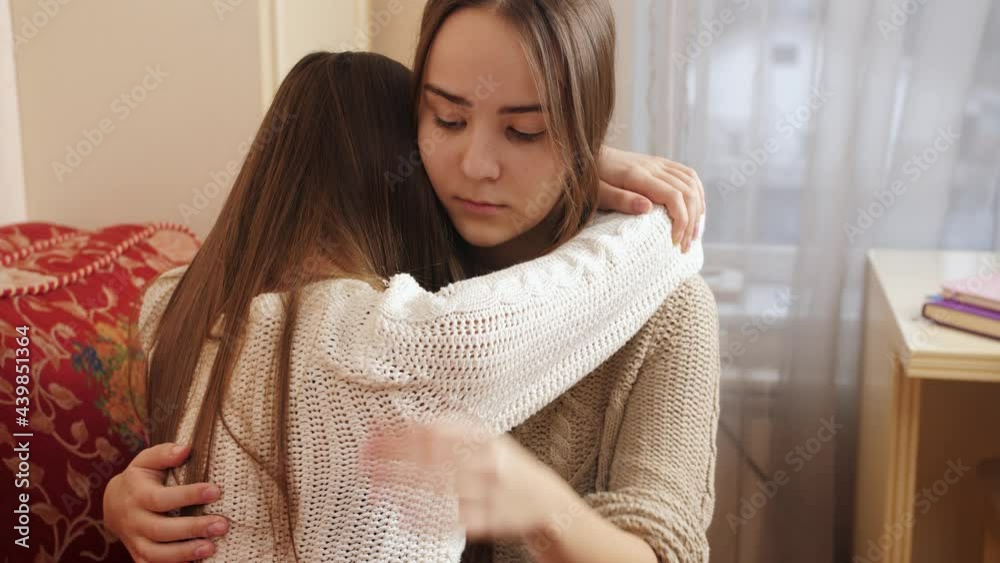 Teenage girl hugging and consoling her crying friend at bedroom ...