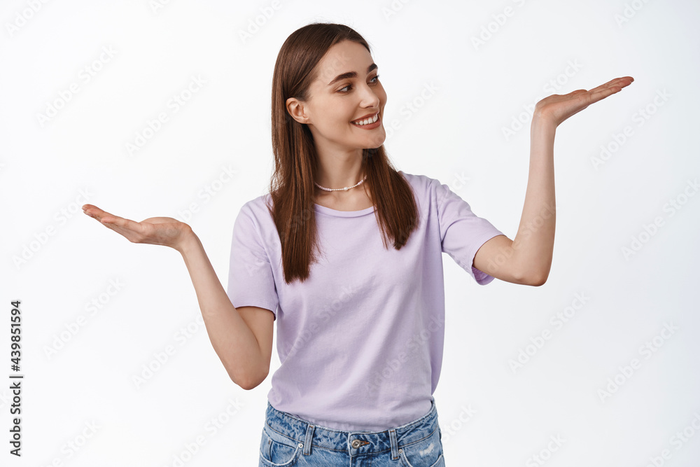 Judging, decision and people concept. Smiling woman holding in open hands, looking at one palm as if choose an item, shopping, weighing something, white background Judging, decision and people concept. Smiling woman holding in open hands, looking at one palm as if choose an item, shopping, weighing something, white background