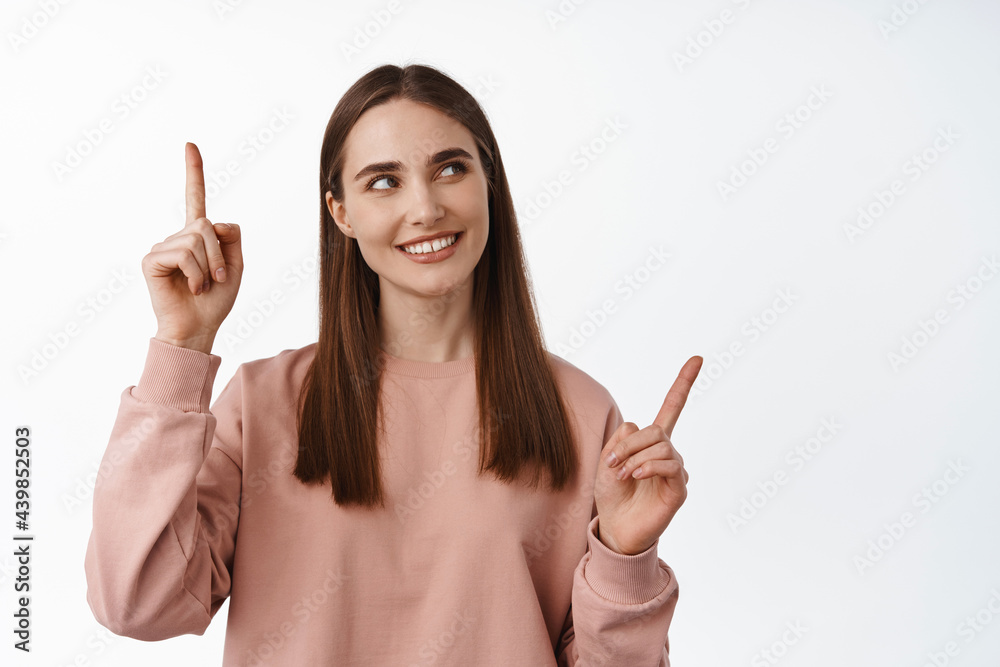 Portrait of beautiful girl choosing, pointing sideways and looking at product logo, smiling thoughtful, makes decision, thinking, standing against white background Portrait of beautiful girl choosing, pointing sideways and looking at product logo, smiling thoughtful, makes decision, thinking, standing against white background
