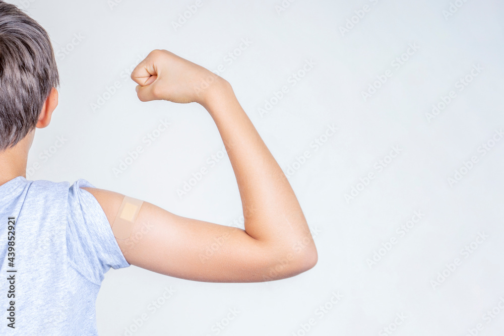 Obraz premium Teenage boy with bandage plaster on his arm makes fist and flexes her bicep after vaccination. Injection covid vaccine, healthcare for children