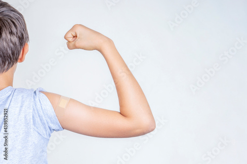Teenage boy with bandage plaster on his arm makes fist and flexes her bicep after vaccination. Injection covid vaccine, healthcare for children