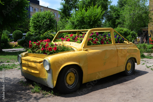 Retro car of yellow color with flowers, a flower bed from the car in the park.  © Mariia