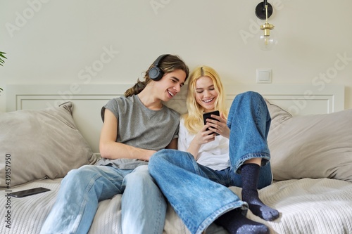 Happy laughing hipster teenagers male and female having fun using smartphone together
