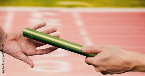 Mid section of hand passing a baton against sports field in background photo