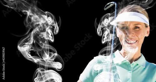 Senior caucasian female golf player holding golf club against smoke effect on black background