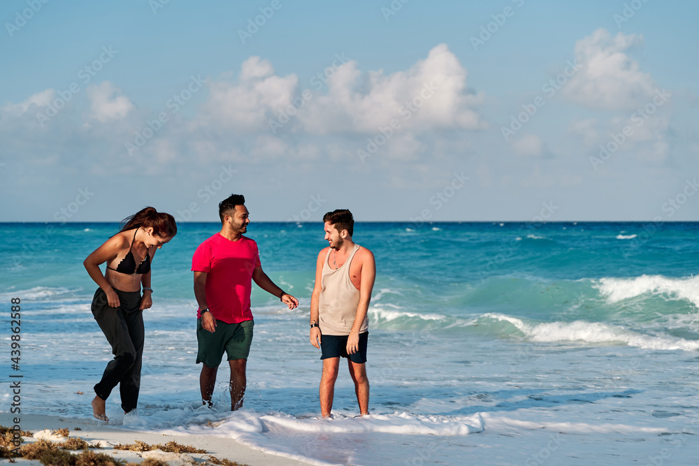 group of three friends, two men and a woman, playing and walking along the coast of cancun beach, rivera maya, with a turquoise sea in the background