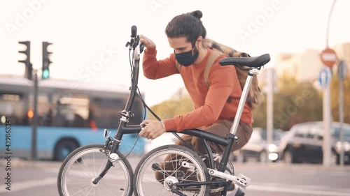 Stock video of man wearing face mask folding his bike in the street.