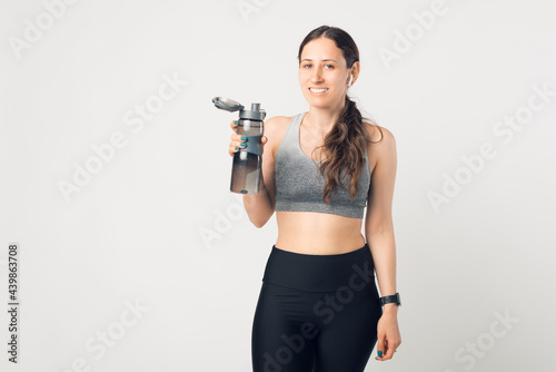 Portrait of sport woman in sportswear standing over white background and holding water bottle