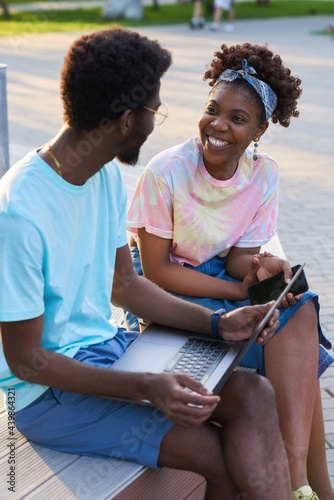 Happy African couple talking to each other and working on laptop outdoors