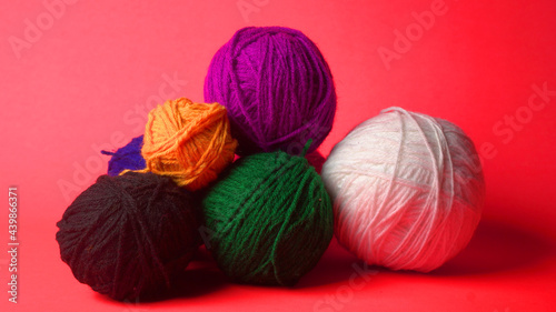 A Piece of knitting with color threads ball of yarn and a knitting needle on red background.