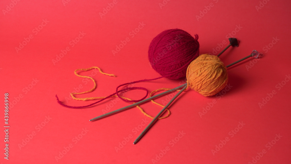 A Piece of knitting with color threads ball of yarn and a knitting needle on red background. A Piece of knitting with color threads ball of yarn and a knitting needle on red background.