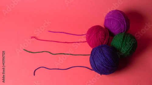 A Piece of knitting with color threads ball of yarn and a knitting needle on red background.