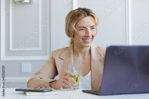 Portrait of a business woman in a suit working on a laptop and drinking lemonade 