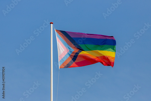 Worldwide LGBTQ community concept with progress pride flag (new design of rainbow flag) waving in the air with blue sky, Celebration of gay pride, The symbol of lesbian, gay, bisexual and transgender.