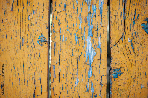 Wood texture with yellow flaked paint. Peeling paint on weathered wood. Old cracked paint pattern on rusty background. Chapped paint on an old wooden surface