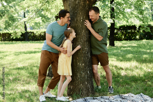 Gay male couple playing with their adopted daughter outdoors in the park