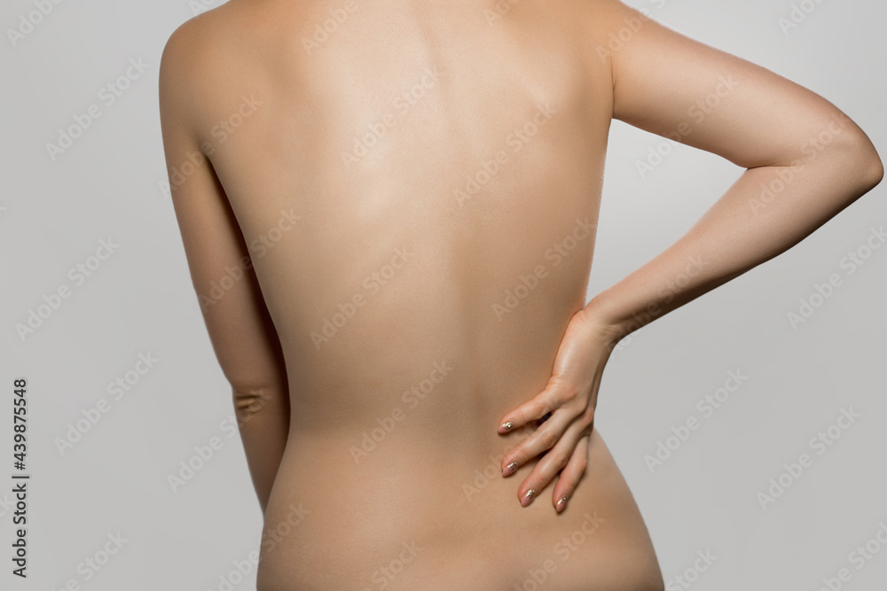 Woman having backache, pain back isolated on gray background. Scoliosis. Spinal cord problems on womans back. Beautiful naked woman touching her back. Woman having backache, pain back isolated on gray background. Scoliosis. Spinal cord problems on womans back. Beautiful naked woman touching her back.